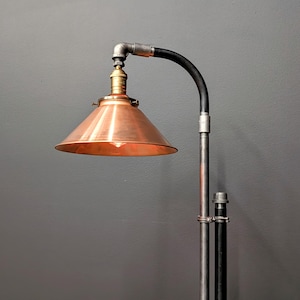 May include: A floor lamp with a copper-colored shade and a black and silver pipe design.