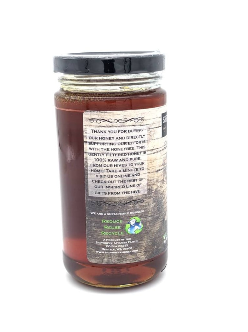 May include: A glass jar of honey with a black lid. The label is brown with white text that reads "Thank you for buying our honey and directly supporting our efforts with the honeybee. This gently filtered honey is 100% raw and pure, from our hives to your home. Take a minute to visit us online and check out the rest of our inspired line of gifts from the hive."