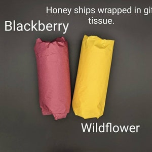 May include: Two rolls of tissue paper wrapped in gift wrap. One roll is burgundy and labeled "Blackberry". The other roll is yellow and labeled "Wildflower".
