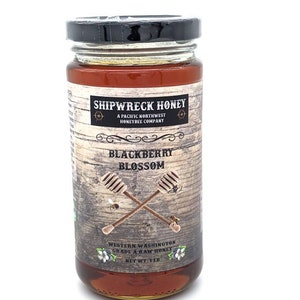 May include: A glass jar of Shipwreck Honey Blackberry Blossom honey. The jar is labeled with a rustic wooden background and the text "Shipwreck Honey, A Pacific Northwest Honeybee Company, Blackberry Blossom, Western Washington Grade A Raw Honey, Net Wt: 1 lb."