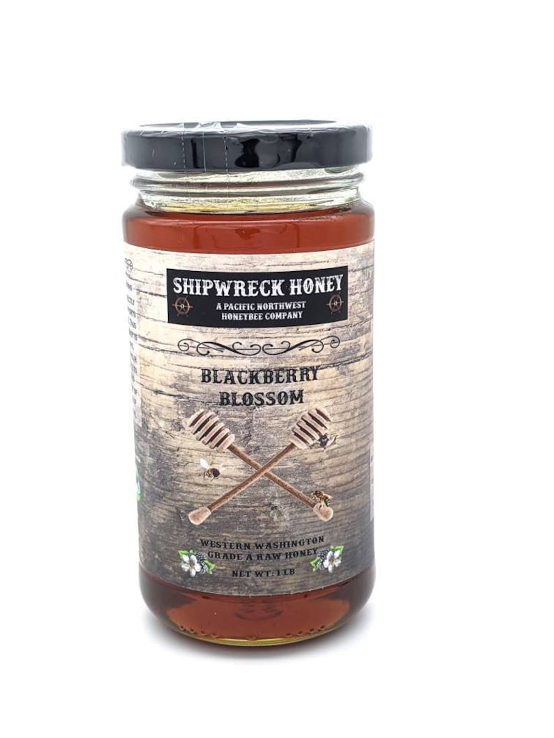May include: A glass jar of Shipwreck Honey Blackberry Blossom honey. The jar is labeled with a rustic wooden background and the text "Shipwreck Honey, A Pacific Northwest Honeybee Company, Blackberry Blossom, Western Washington Grade A Raw Honey, Net Wt: 1 lb."