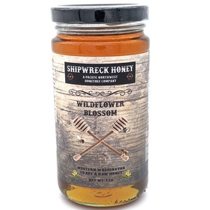 May include: A glass jar of Shipwreck Honey Wildflower Blossom honey. The jar has a black lid and a brown label with white text. The label says "Shipwreck Honey", "A Pacific Northwest Honeybee Company", "Wildflower Blossom", "Western Washington Grade A Raw Honey", and "Net Wt: 1 lb".