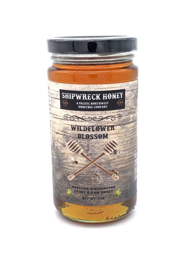 May include: A glass jar of Shipwreck Honey Wildflower Blossom honey. The jar has a black lid and a brown label with white text. The label says "Shipwreck Honey", "A Pacific Northwest Honeybee Company", "Wildflower Blossom", "Western Washington Grade A Raw Honey", and "Net Wt: 1 lb".