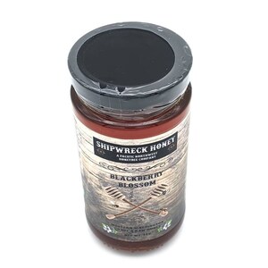 May include: A glass jar of Shipwreck Honey Blackberry Blossom honey. The jar has a black lid and a brown label with white text. The label says "Shipwreck Honey, A Pacific Northwest Honeybee Company, Blackberry Blossom, Western Washington, Unheated & Raw Honey, Net Wt 12 oz."