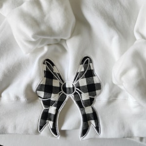 May include: White sweatshirt with a black and white checkered bow applique.