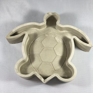 May include: A gray concrete turtle planter with a textured shell design. The planter is shaped like a turtle with a hollow center for planting.