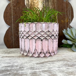 May include: A pink geometric planter with a distressed finish. The planter is filled with a green succulent plant.