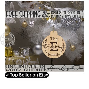 May include: Unfinished wooden ornament with the text "The Edwards Family" in a circle with a large "E" and leafy branches. The ornament is on a Christmas tree with other ornaments and presents.