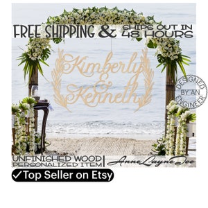 Könnte beinhalten: Ein hölzernes Hochzeitsschild mit den Namen Kimberly und Kenneth in Kursivschrift. Das Schild hängt an einem Blumengang an einem Strand. Das Schild ist unbehandelt und kann personalisiert werden. Der Text "Versand innerhalb von 48 Stunden" und "Topseller auf Etsy" ist ebenfalls sichtbar.