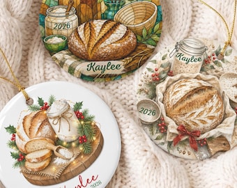 May include: Three round ceramic ornaments featuring illustrations of sourdough bread, flour jars, and baking tools. Each ornament displays the name Kaylee and the year 2026. The designs include stained glass patterns, festive greenery, and red berries.