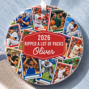 May include: A round ceramic ornament featuring a collage of various sports action photographs, including baseball and football players. A central red hexagonal label displays the white text 2026 RIPPED A LOT OF PACKS and the name Oliver.