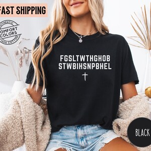 Puede incluir: Camiseta negra con texto blanco y una cruz. El texto dice "FGSLTWTHGHOB STWBIHSNPBHEL". La camiseta es 100% algod&oacute;n y presenta una pancarta de "Env&iacute;o r&aacute;pido".