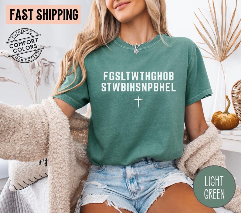 Puede incluir: Camiseta verde claro con texto blanco y una cruz. La camiseta tiene el texto "FGS LTWTHGHOB STWBIHSNPBHEL" impreso en la parte delantera. La camiseta es 100% algod&oacute;n y es de color c&oacute;modo.
