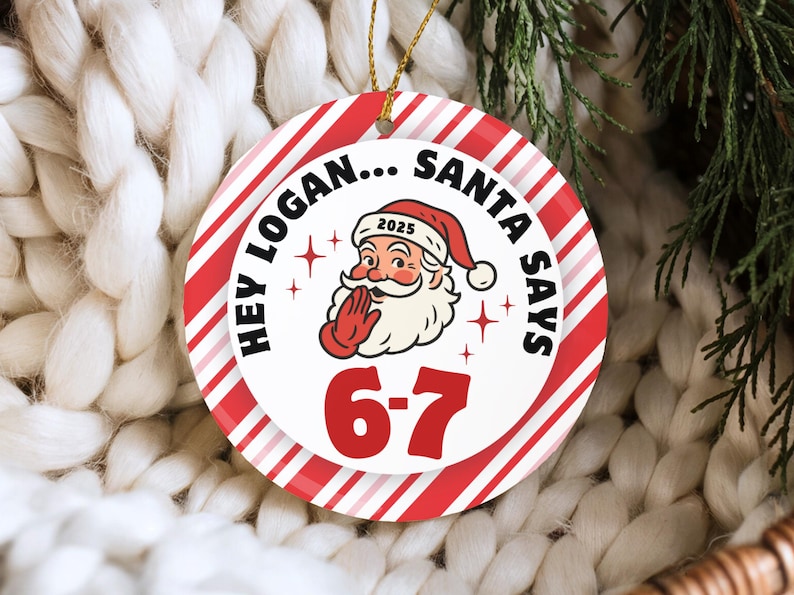 May include: A round Christmas ornament with a red and white striped border. The center features Santa Claus with the text "HEY LOGAN... SANTA SAYS" and the numbers "6-7". The ornament is hanging by a gold string.