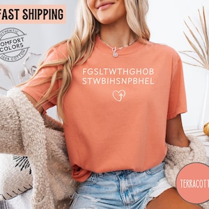 May include: Terracotta-colored t-shirt with white text and a heart with a cross graphic. The shirt has short sleeves and is made of 100% cotton. The words "FAST SHIPPING" are at the top of the image.