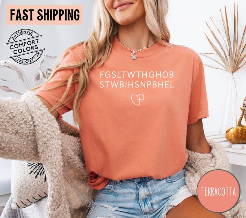 May include: Terracotta-colored t-shirt with white text and a heart with a cross graphic. The shirt has short sleeves and is made of 100% cotton. The words "FAST SHIPPING" are at the top of the image.