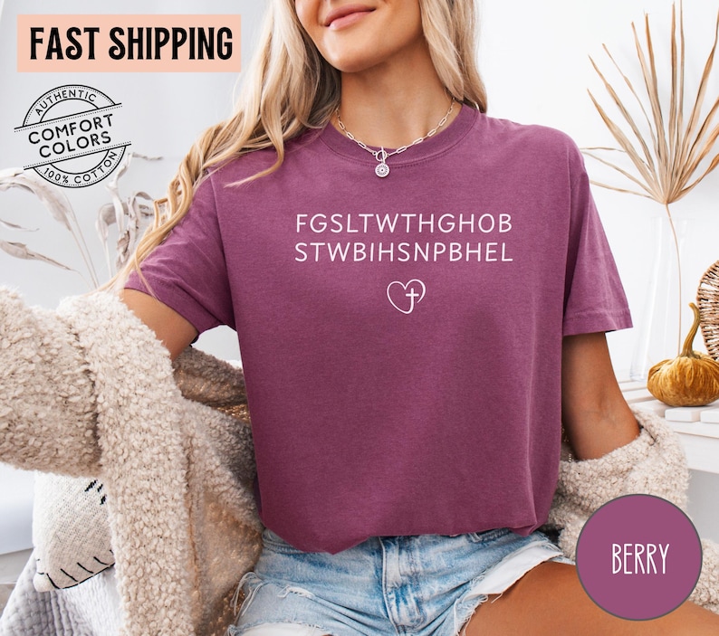 May include: Berry-colored t-shirt with white text and a heart-shaped cross design. The shirt has a relaxed fit and is made of a soft material. The shirt also has the text "FAST SHIPPING" and "AUTHENTIC COMFORT COLORS 100% COTTON" on the top left.