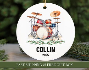 May include: White ceramic ornament featuring a watercolor illustration of a drum set with red, orange, and blue drums and cymbals. The name "COLLIN" and the year "2025" are printed in black. A green and red garland decorates the bottom.