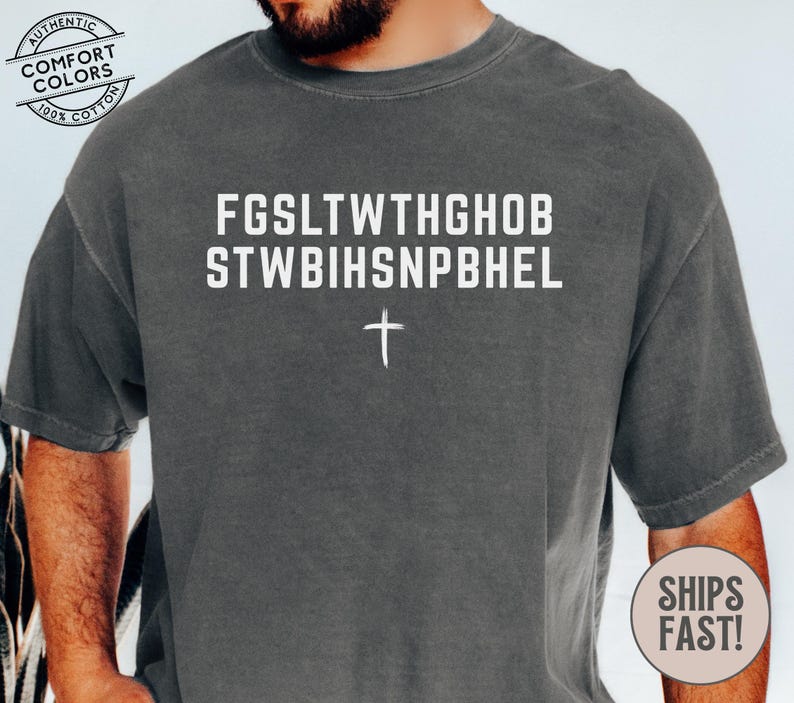 Puede incluir: Una camiseta de manga corta gris carb&oacute;n con el texto blanco FGSLTWTHGHOB STWBIHSNPBHEL y un peque&ntilde;o s&iacute;mbolo de cruz blanca debajo. La camiseta tiene cuello redondo y un corte relajado con un aspecto lavado de estilo vintage.