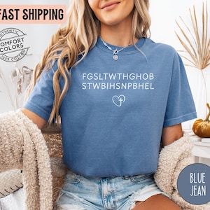 May include: Blue jean-colored t-shirt with white text and a heart with a cross graphic. The shirt has the words "AUTHENTIC COMFORT COLORS 100% COTTON" printed on it. The words "FAST SHIPPING" are printed on the top left of the image.