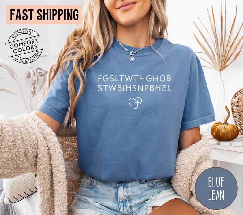 May include: Blue jean-colored t-shirt with white text and a heart with a cross graphic. The shirt has the words "AUTHENTIC COMFORT COLORS 100% COTTON" printed on it. The words "FAST SHIPPING" are printed on the top left of the image.