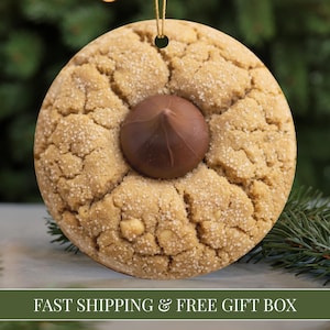 May include: Round Christmas ornament resembling a peanut butter cookie with a chocolate candy center. The ornament is tan with a textured surface and a gold string for hanging. The text "FAST SHIPPING & FREE GIFT BOX" is at the bottom.