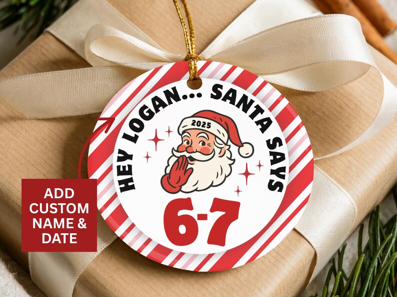 May include: A round Christmas ornament with a red and white striped border. The ornament features Santa Claus with the text "HEY LOGAN... SANTA SAYS" and "6-7". The year "2025" is on Santa's hat. A gold string is attached.