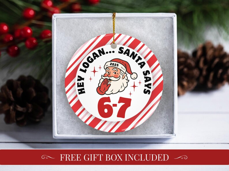 May include: A round Christmas ornament with a red and white striped border. The ornament features Santa Claus with the text "HEY LOGAN... SANTA SAYS 6-7 2025". The ornament is in a white gift box.
