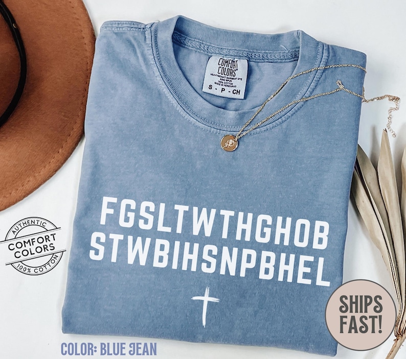 Puede incluir: Camiseta Comfort Colors azul vaquero con texto blanco y un gr&aacute;fico de cruz. La camiseta tiene cuello redondo y mangas cortas. Un collar dorado con un colgante est&aacute; sobre la camiseta. La camiseta es 100% algod&oacute;n.