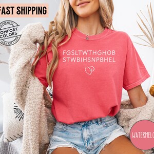 May include: A watermelon-colored t-shirt with white text and a heart with a cross graphic. The shirt has short sleeves and a relaxed fit. The words "FAST SHIPPING" and "AUTHENTIC COMFORT COLORS 100% COTTON" are also visible.