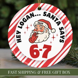 May include: A round Christmas ornament with a red and white striped border. The center features Santa Claus with the text "HEY LOGAN... SANTA SAYS" and the numbers "6-7". The year "2025" is on Santa's hat. A gold string is attached.