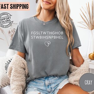 May include: Gray t-shirt with white text and a heart-shaped symbol. The shirt has the words "AUTHENTIC COMFORT COLORS 100% COTTON" printed on it. The shirt is made of a soft, comfortable material.