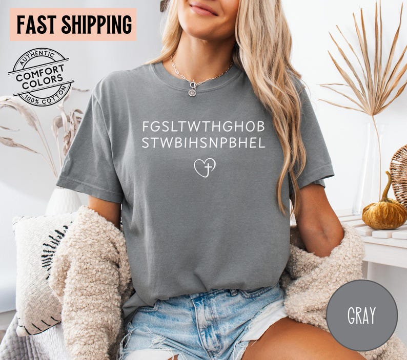 May include: Gray t-shirt with white text and a heart-shaped symbol. The shirt has the words "AUTHENTIC COMFORT COLORS 100% COTTON" printed on it. The shirt is made of a soft, comfortable material.