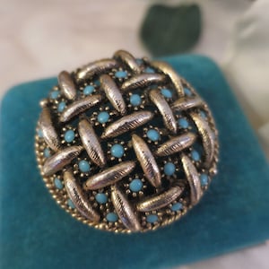May include: A gold-toned brooch with a woven design and turquoise blue stones.