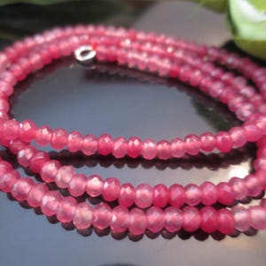 May include: A necklace featuring three strands of small, faceted, pink gemstones. The beads are strung together, creating a delicate and elegant piece of jewellery. The necklace is displayed on a reflective surface.