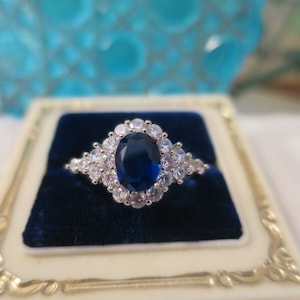 May include: A silver ring featuring a large oval blue sapphire surrounded by smaller clear stones.