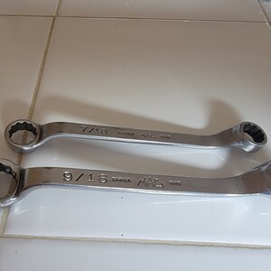 May include: Two silver wrenches with black markings. The top wrench is labeled "7/16" and the bottom wrench is labeled "9/16". Both wrenches are labeled "MAC" and "SAGINAW".