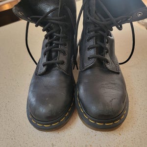 May include: A pair of black leather ankle boots with yellow stitching and black laces. The boots have a worn look.