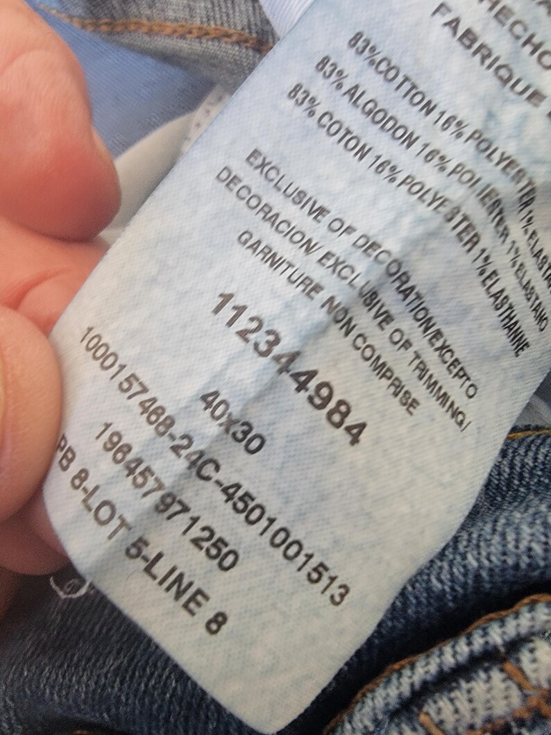 K&ouml;nnte beinhalten: Nahaufnahme eines wei&szlig;en Kleidungsetiketts mit schwarzem Text. Das Etikett zeigt die Zahlen "112344984" und "40x30". Die Stoffzusammensetzung ist mit 83% Baumwolle, 16% Polyester und 1% Elasthan angegeben.