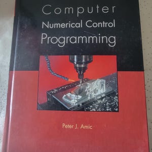 May include: A book titled "Computer Numerical Control Programming" with a black and red cover. The cover features an image of a CNC machine in operation. The author's name, Peter J. Amic, is printed at the bottom.