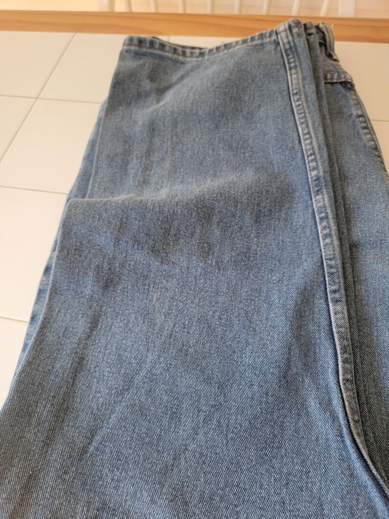 Puede incluir: Vaqueros de mezclilla azul claro, doblados. Los vaqueros tienen un dise&ntilde;o cl&aacute;sico de cinco bolsillos, cremallera y corte recto. La tela muestra una sutil decoloraci&oacute;n y desgaste.