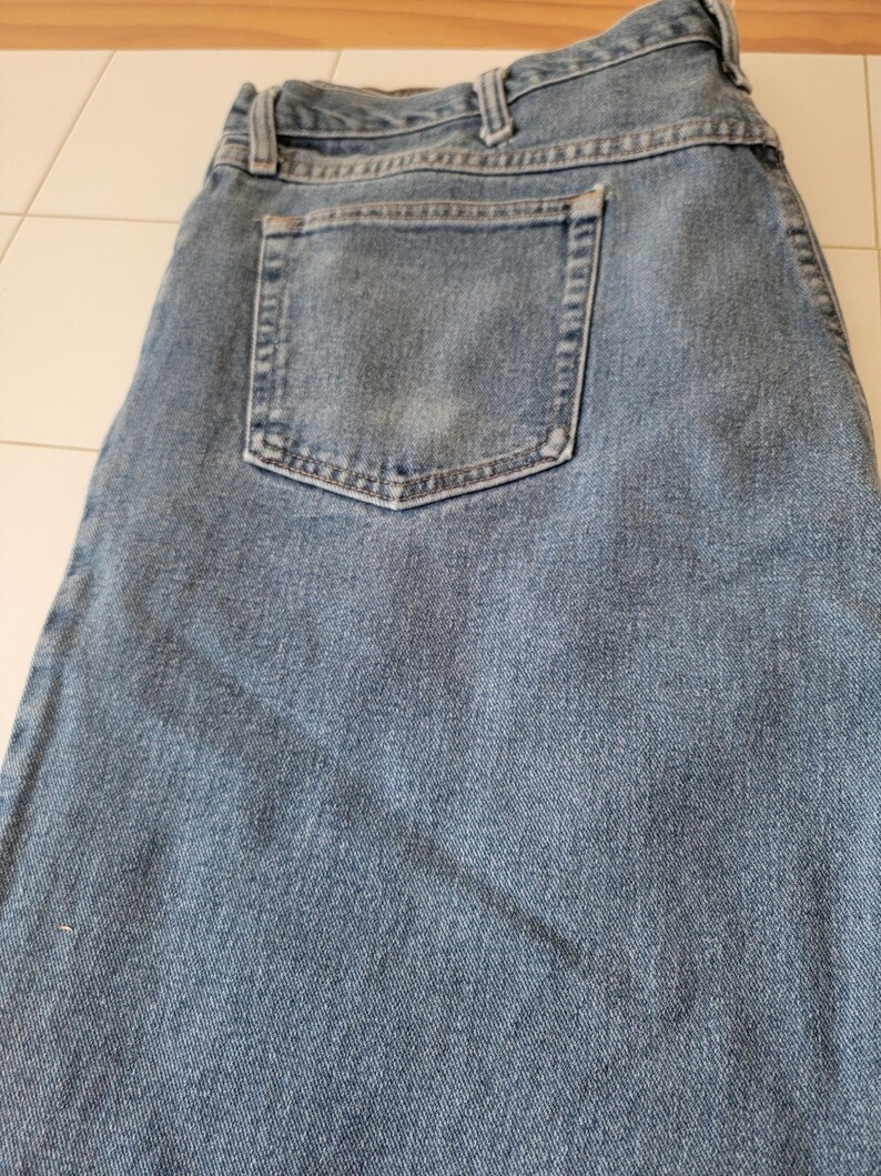 Puede incluir: Vaqueros de mezclilla azul claro con un dise&ntilde;o cl&aacute;sico de cinco bolsillos. Los vaqueros tienen un aspecto descolorido y un solo bolsillo trasero. La tela muestra signos de desgaste, lo que se suma a la est&eacute;tica informal. Los vaqueros est&aacute;n doblados.