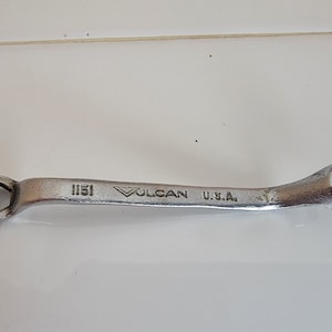 May include: A silver wrench with a curved handle. The wrench is labeled "1151 VULCAN U.S.A."