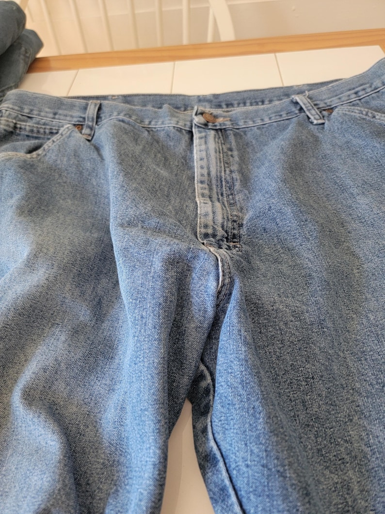 May include: Light blue denim jeans with a button closure and belt loops. The jeans have a classic five-pocket design and a faded wash. The fabric appears to be a medium weight denim.
