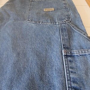 May include: Light blue denim jeans with multiple pockets, including a large carpenter pocket on the side. The back pocket features a small, rectangular "Wrangler" label. The jeans are made of a durable denim fabric.
