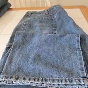 May include: Light blue denim jeans with a classic five-pocket design. The jeans are folded, showcasing the front pockets, belt loops, and the texture of the denim fabric. The jeans appear to be a relaxed fit.