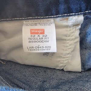 May include: Close-up of a Wrangler jeans label. The label is white with black text, indicating size 42 x 32, regular fit. The jeans are made in Mexico of US fabric, with 80% cotton and 20% polyester.