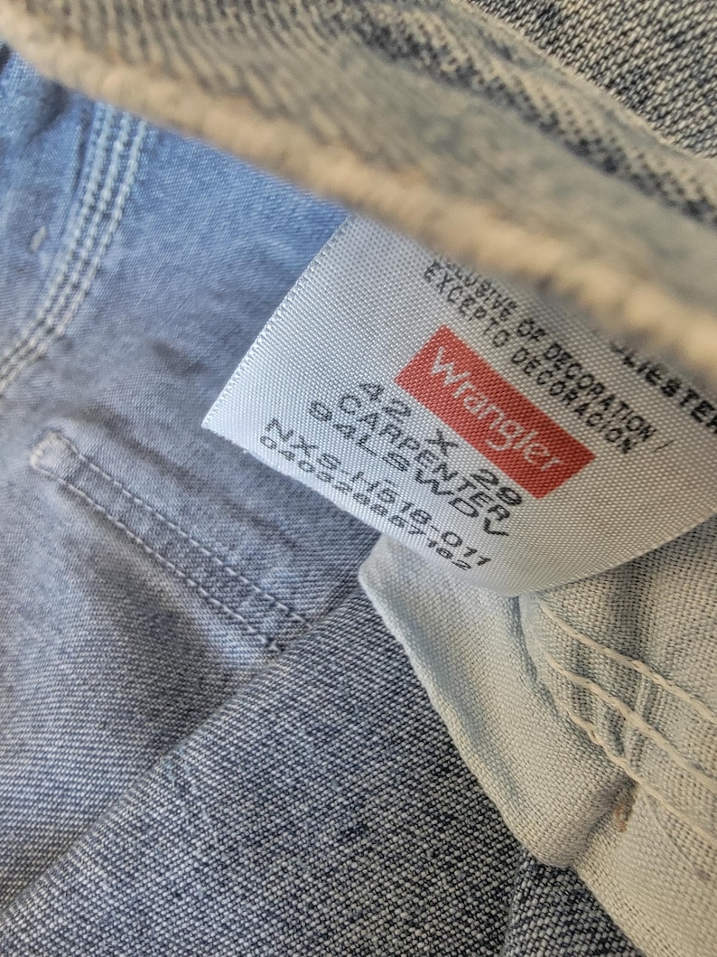 May include: Close-up of a Wrangler jeans tag. The tag is white with red lettering and text that reads "Wrangler 42 X 29 Carpenter 94LSWDV". The jeans are light blue denim.