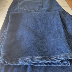 May include: Dark blue denim jeans with a classic five-pocket design. The jeans are folded, showcasing the back pocket and the hem. The fabric appears to be a medium weight, suitable for everyday wear.