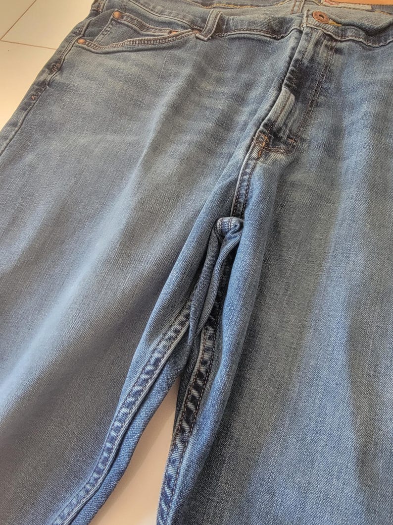 K&ouml;nnte beinhalten: Nahaufnahme einer hellblauen Jeans. Die Jeans hat ein klassisches F&uuml;nf-Taschen-Design, einen Knopf- und Rei&szlig;verschluss und eine verwaschene Optik. Die N&auml;hte sind entlang der N&auml;hte und Taschen sichtbar.
